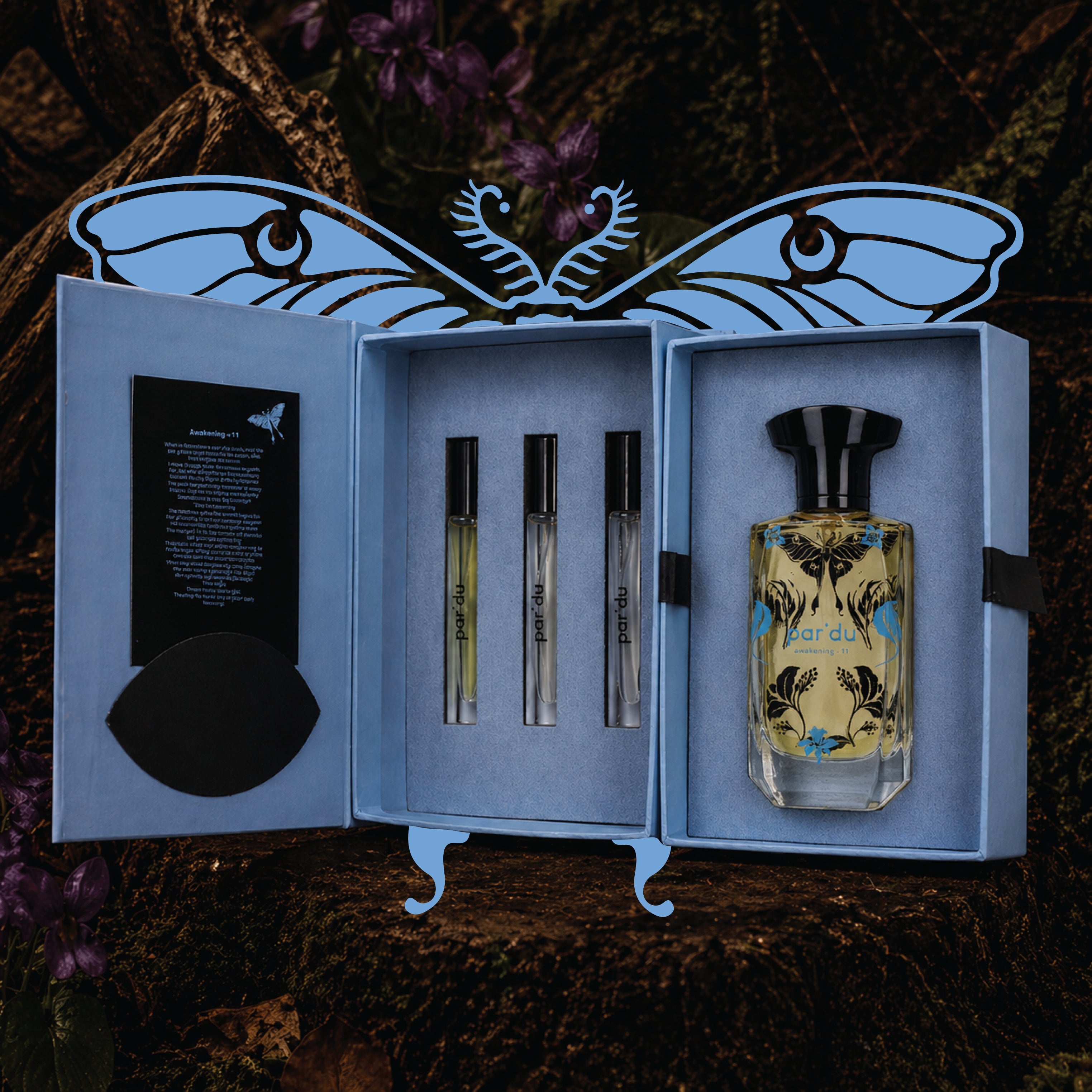 Perfume set with three bottles and a larger bottle in an open box, featuring butterfly design on a dark background.